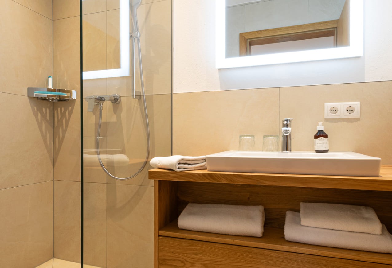 Badezimmer mit Waschbecken, beleuchtetem Spiegel und Dusche